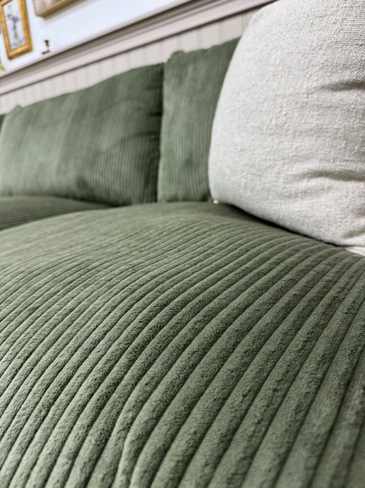 Close-up of a green sofa with a neutral pillow.